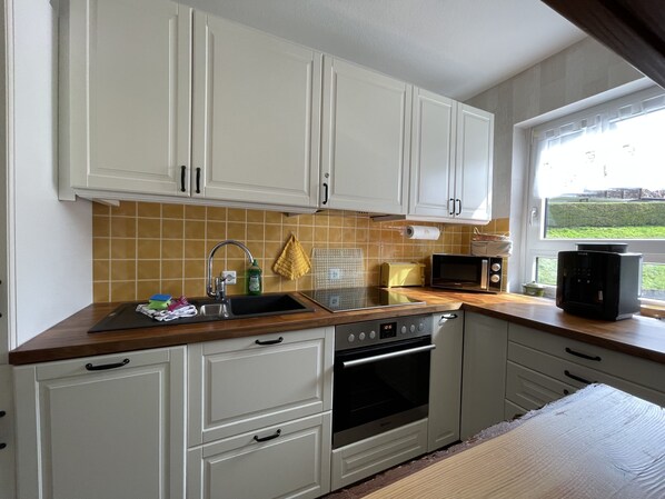 A compact kitchen with white cabinets, a stainless steel sink, a microwave, and a built-in oven. - Cozy, sunny apartment with swimming pool, sauna, W-lan, Feldberg view (Lenzkirch)