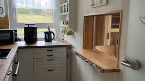 Une cuisine compacte avec des meubles blancs, un micro-ondes posé sur le plan de travail, une machine à café et une fenêtre donnant sur un espace verdoyant.