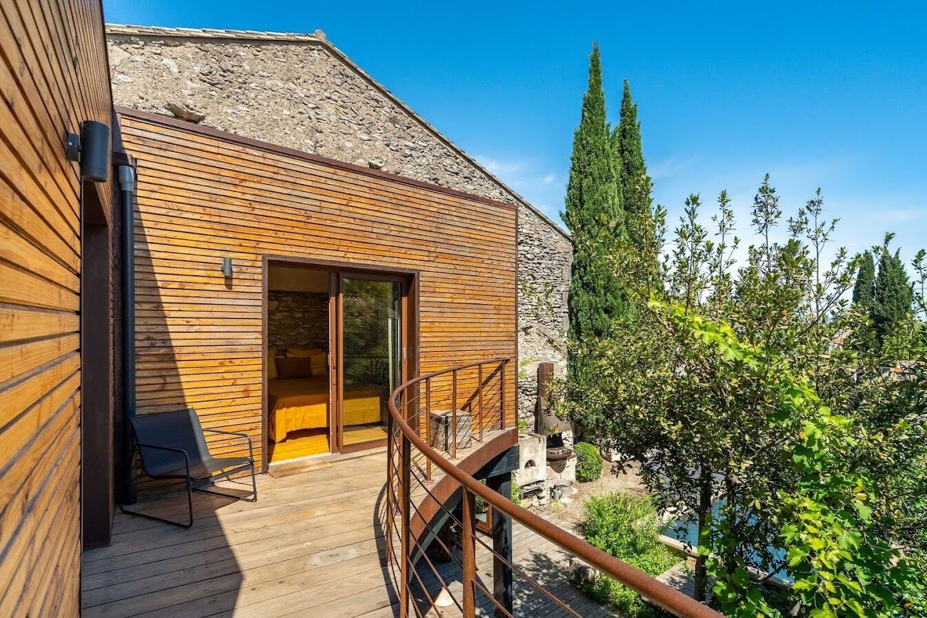 A wooden exterior with a stone wall, a wooden deck, and a staircase leading to a glass door.