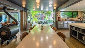 Une cuisine moderne dotée d’une longue table à manger, d’appareils électroménagers intégrés et de grandes fenêtres offrant une vue sur l’extérieur.