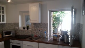 Cozinha com micro-ondas, fogão, pia e armários. Há uma janela com plantas no parapeito.