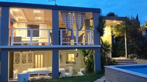 Uma casa de dois andares com varanda, área de jantar e piscina.