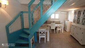 Uma escadaria com corrimãos turquesa, um espaço de refeições com mobiliário branco e um armário branco com portas de vidro.