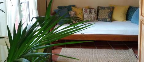 A bedroom with a bed, a large window with curtains, a floor lamp, a painting on the wall, and a potted plant.