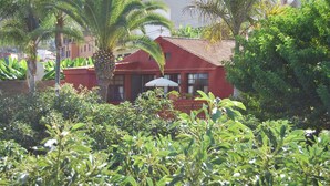 A red building with a tiled roof surrounded by lush greenery, including palm trees and various plants. - Light-flooded country house with WiFi connection * Last minute offer * (La Orotava)