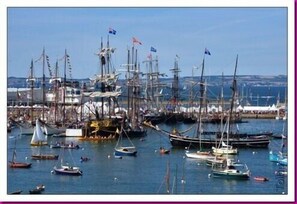 Boats docked in a marina with piers and flags, set against a coastal town backdrop.
