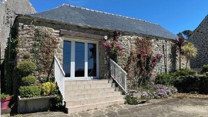 Un bâtiment en pierre doté d’un toit en pente, une entrée principale avec une porte blanche et un petit escalier menant à l’entrée.