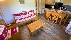 Un saló acollidor amb un sofà, una taula de dinar de fusta i cadires. Es pot veure una cuina amb microones i fogons al fons.