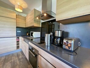 A modern kitchen with wooden cabinets, a microwave, a coffee maker, and a toaster. - Spacious Ski-In/Ski-Out Apartment for 6 with Balcony and Stunning Views (Les Menuires)