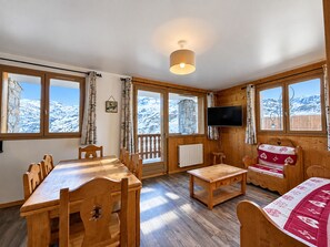 A wooden interior with a dining table, chairs, a sofa, and a television. - Spacious Ski-In/Ski-Out Apartment for 6 with Balcony and Stunning Views (Les Menuires)