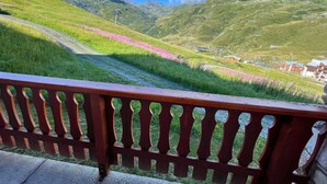 Una vista panoràmica des d'un balcó amb barana de fusta, sobre un paisatge amb turons verds i una petita població.