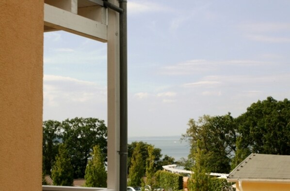 A balcony with a view of the sea and surrounding greenery.