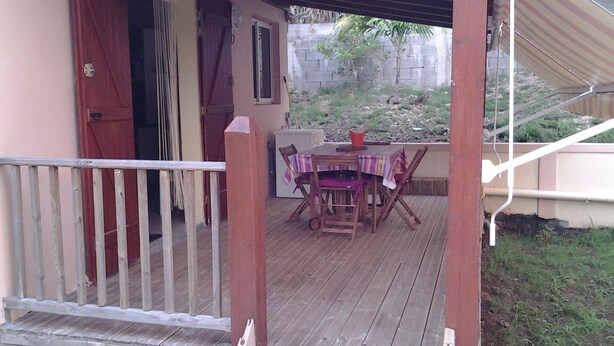 Un terrazzo in legno con tavolo e sedie, una porta e un piccolo giardino.