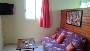 Una stanza con un divano in legno, un tavolino, una TV a parete e una finestra con tende.