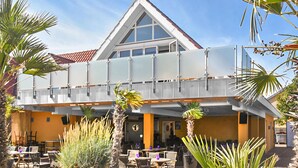A hotel with a modern design, featuring a prominent triangular roof, large windows, and outdoor seating area with palm trees.