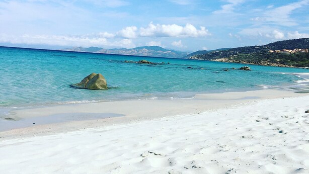 Ein Strand mit klarem türkisblauem Wasser, weißem Sand und Felsformationen.