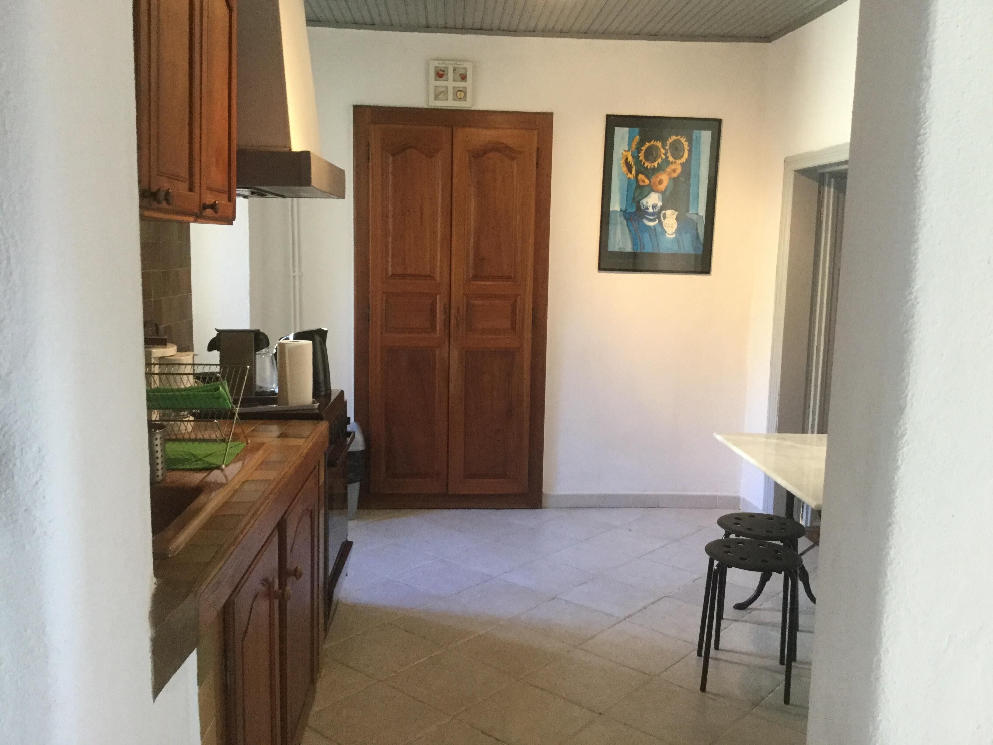 Une petite cuisine avec des meubles en bois, un sol carrelé, une porte à deux battants et un tableau accroché au mur.