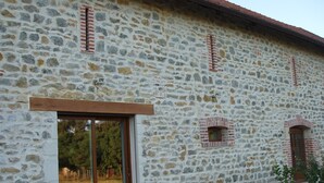 A stone building with a wooden-framed window and a metal table with chairs outside.
