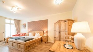 A bedroom with a wooden bed, a nightstand, a desk, a lamp, and a wardrobe. - Comfort room - Aparthotel Waldfrieden (Sellin)