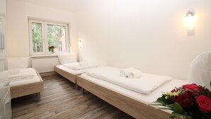 Quarto limpo e minimalista com duas camas, uma janela e uma mesa de cabeceira com um vaso de flores.