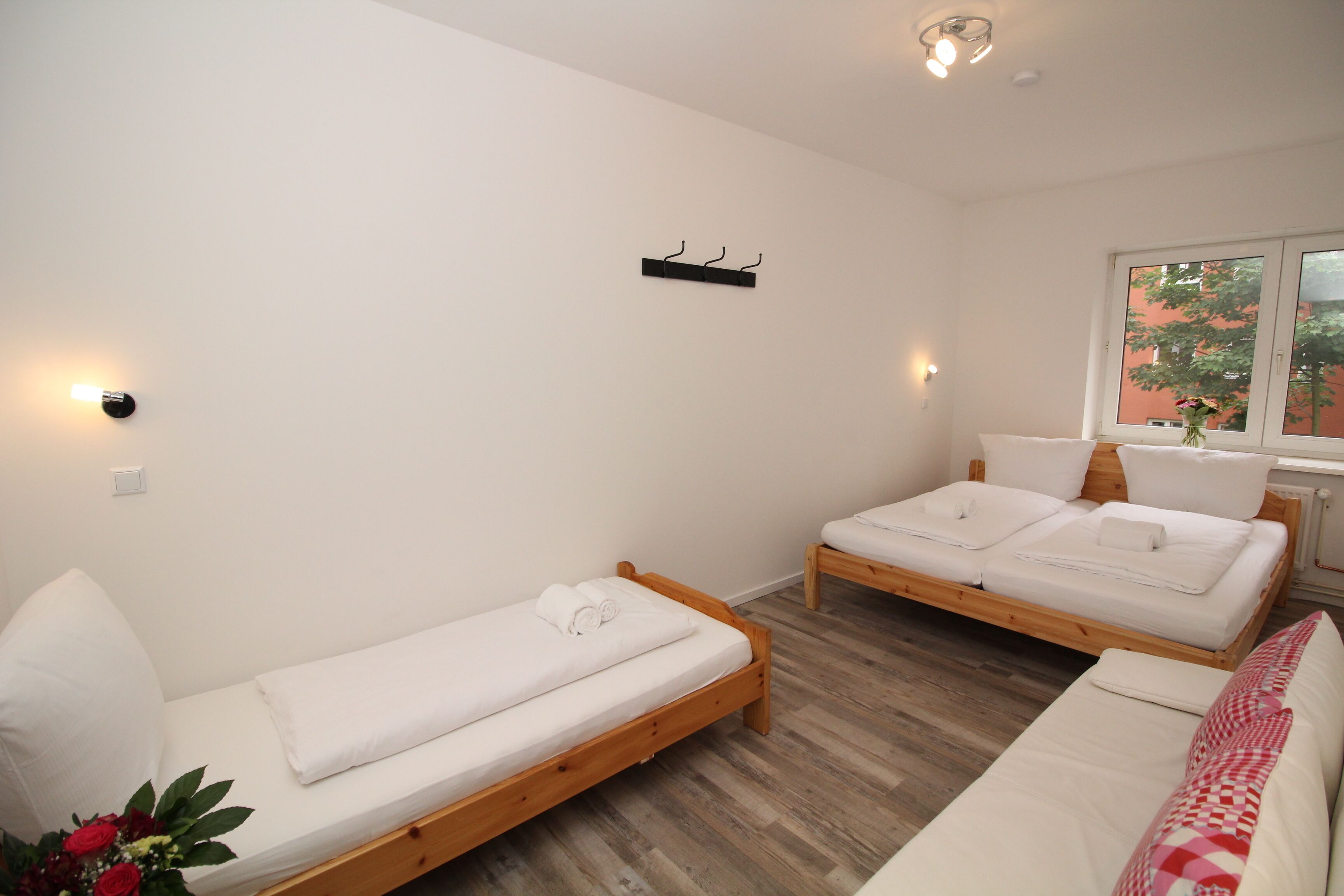 Une chambre avec deux lits en bois, du linge de lit blanc, un plancher en bois, une fenêtre donnant sur un paysage agréable et un luminaire fixé au mur.