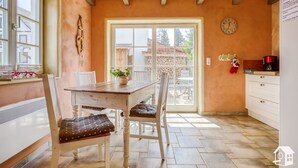 A kitchen with a wooden table, chairs, a clock, and a view through a glass door. - Vacation in a monument; Relax in the Geo-Naturpark Frau-Holle-Land, 4 DTV * (Berkatal-Hitzerode)
