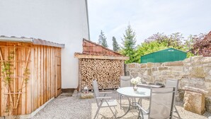 A patio area with a table and chairs, a stack of firewood, a green shed, and a stone wall. - Vacation in a monument; Relax in the Geo-Naturpark Frau-Holle-Land, 4 DTV * (Berkatal-Hitzerode)