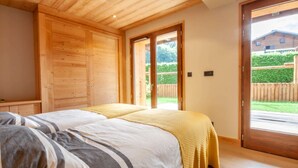 A bedroom with two beds, wooden wardrobe, and a sliding glass door leading to a garden. - K-Terra 4 : Recent and modern chalet with hot tub (MONTRIOND)