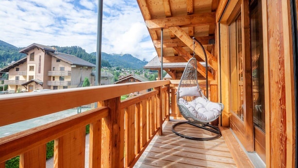 A wooden balcony with a hanging chair, wooden railings, and a view of houses and mountains. - K-Terra 4 : Recent and modern chalet with hot tub (MONTRIOND)