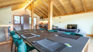 A spacious room with a high wooden ceiling, a long dining table with chairs, a sofa, and a television. - K-Terra 4 : Recent and modern chalet with hot tub (MONTRIOND)