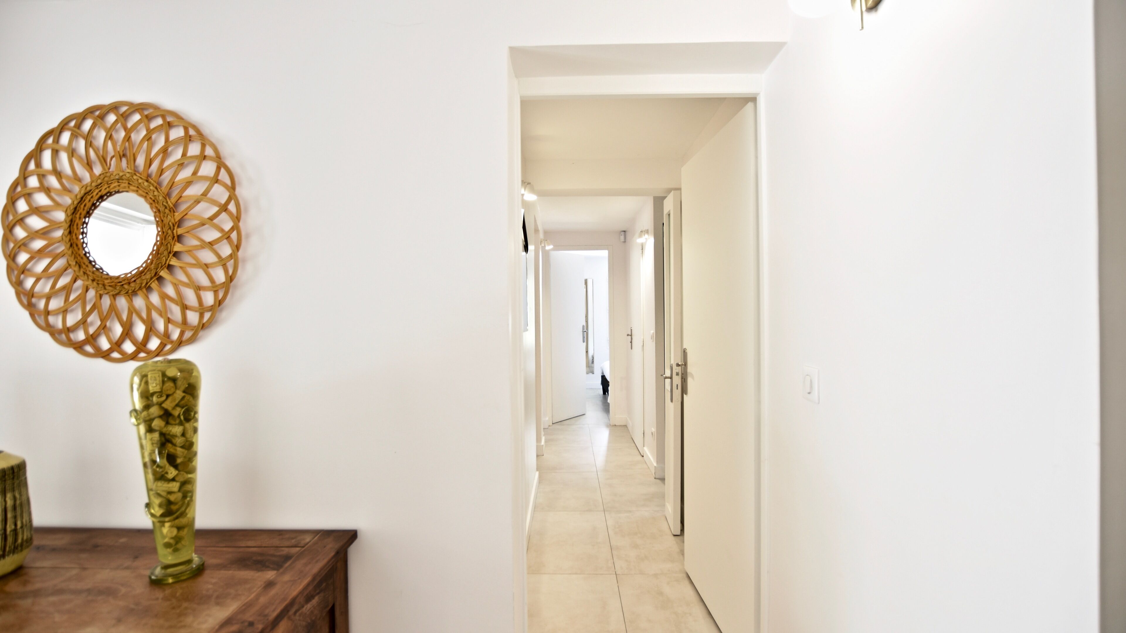 A hallway with a decorative woven wall hanging and a tall, textured vase on a wooden table.