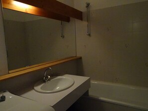 Une salle de bain avec un lavabo blanc, un miroir et une baignoire.