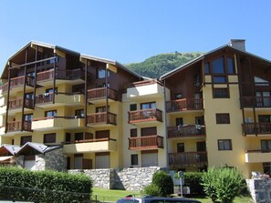 Un hôtel à plusieurs étages doté de balcons, d’une base en pierre et surplombant un paysage montagneux.