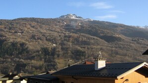 A mountain with a snow-capped peak and a clear sky. There are buildings with sloped roofs in the foreground.