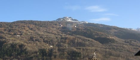 A mountain with a snow-capped peak and a clear sky. There are buildings with sloped roofs in the foreground.