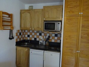 A compact kitchen with wooden cabinets, a microwave, a dishwasher, and a checkered backsplash.