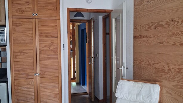 A hallway with wooden paneling, a white chair, and a door leading to another room.
