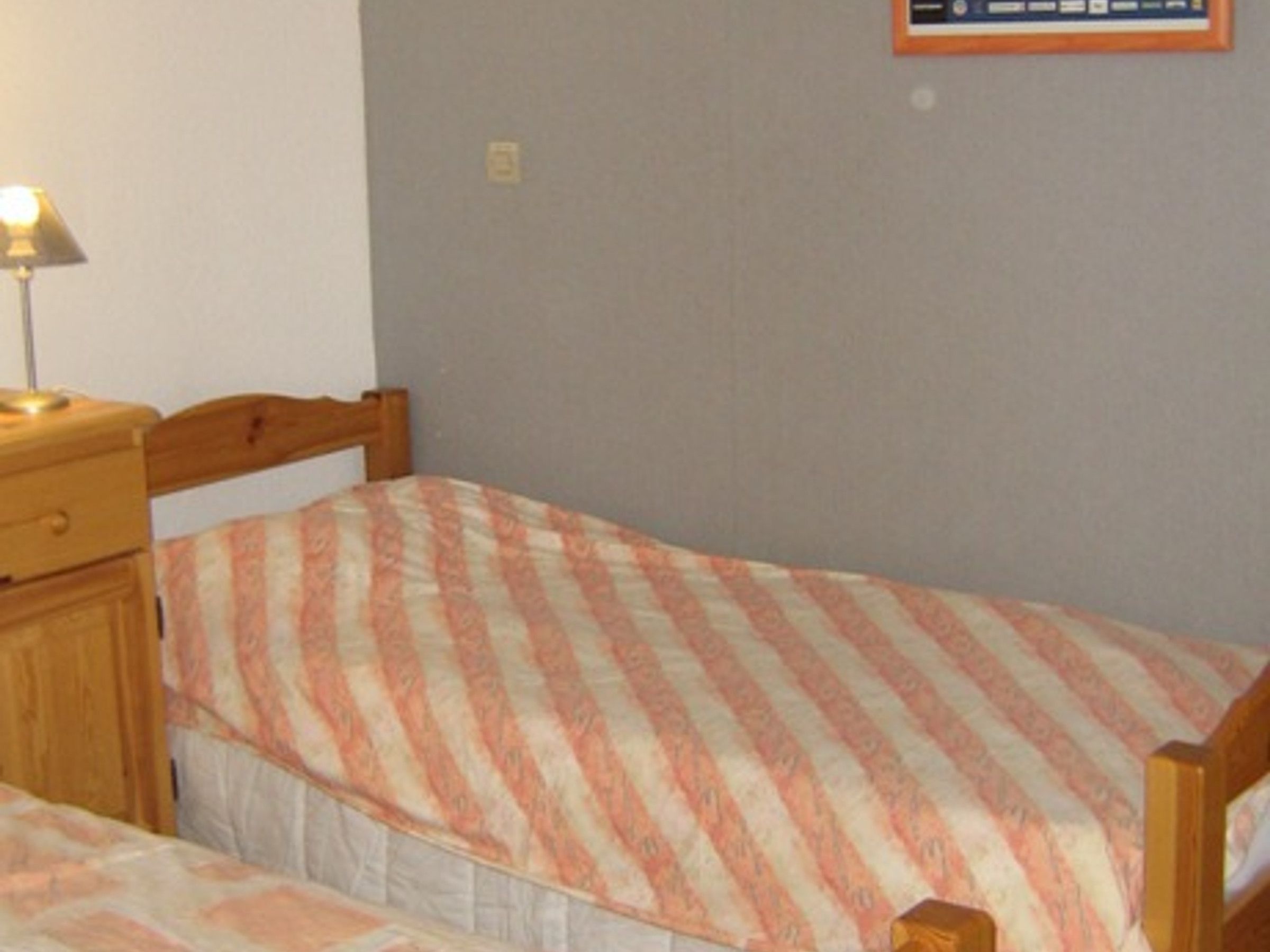 A bedroom with two single beds, a wooden nightstand with a lamp, and a framed picture on the wall.