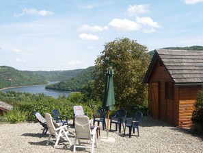 A wooden cabin with a gravel patio, outdoor seating, and a view of a lake and forest. - Large chalet with jacuzzi and lake view (Saint-Jacques-D'ambur)