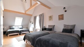 Et soveværelse med to senge, træbjælker, et vindue og et natbord med en lampe.