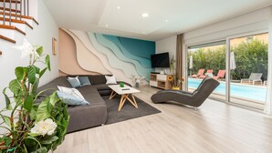 Un salon moderne avec un canapé, une table basse, un téléviseur et une vue sur la piscine.