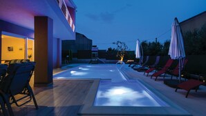 Un espace piscine avec des chaises longues et des parasols, une terrasse en bois et un bâtiment doté de grandes fenêtres.