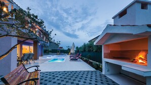 Une terrasse avec une piscine, des chaises longues, un banc en bois et un barbecue.