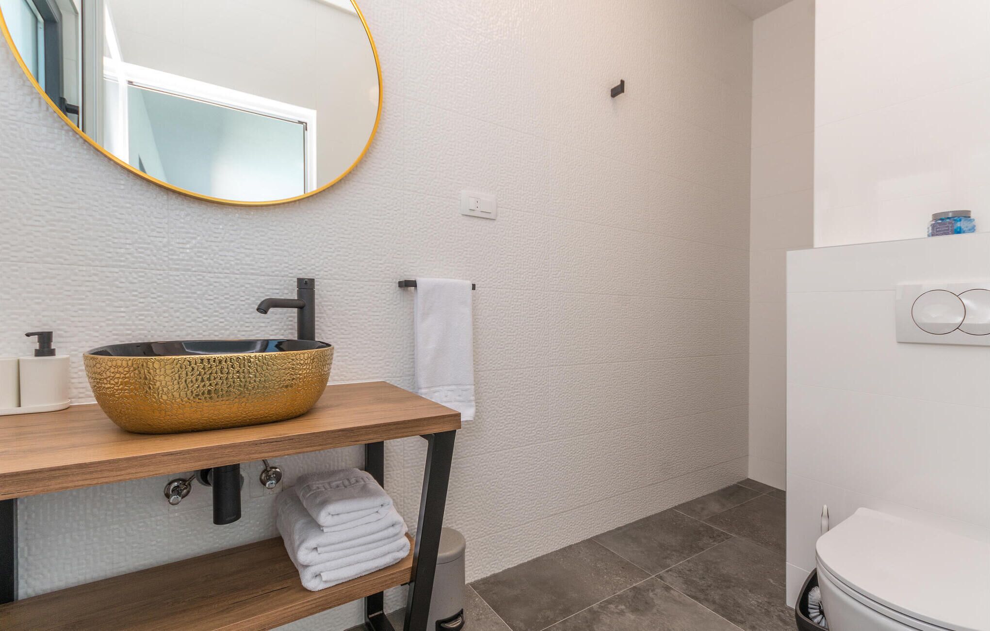 Un bagno con un mobile vanitario in legno, un lavabo con texture dorata, uno specchio con cornice dorata, un porta asciugamani e un water.