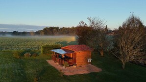 Une petite cabane en bois, surmontée d’un toit en métal, entourée d’un champ herbeux et d’arbres.