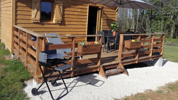 Une cabane en bois dotée d’une terrasse, de meubles d’extérieur, d’un barbecue et d’un grand parasol.