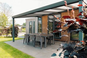A modern outdoor patio with a table and chairs, a covered seating area, and a wooden exterior wall. - 6 person Veluwe villa with sauna (Voorthuizen)