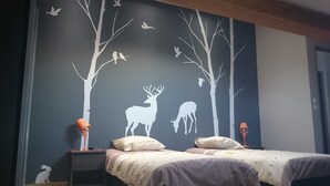 Ein Schlafzimmer mit einem Bett, zwei Nachttischen und einer Wandmalerei von Waldlandschaft mit Hirschen und Vögeln.