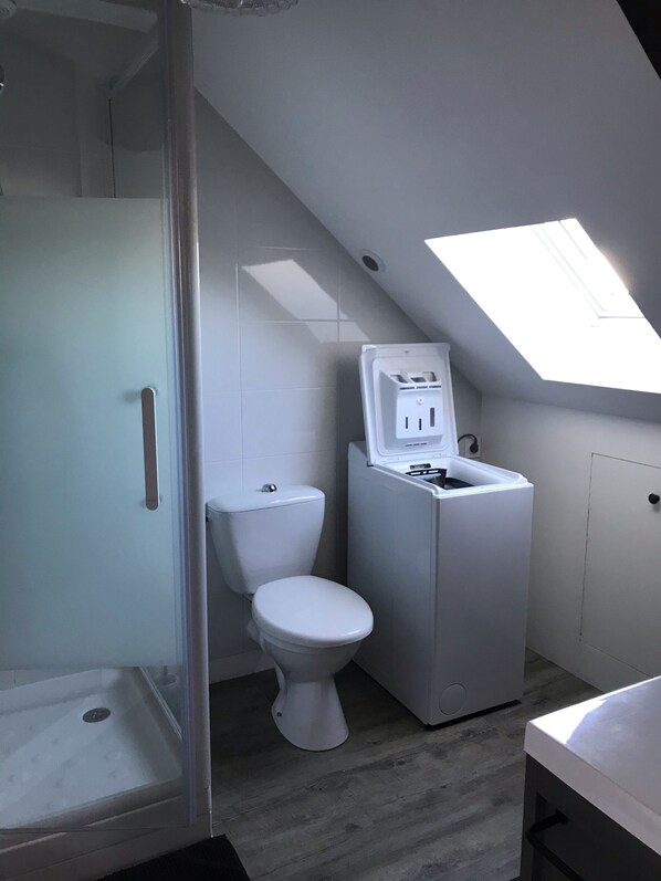Ein kleines Badezimmer mit Dusche, Toilette und integriertem Waschmaschinenanschluss.