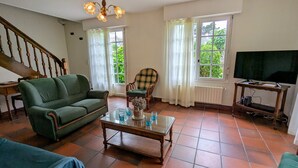 Una sala de estar con un sofá verde, una mesa de centro de cristal, un sillón escocés y un televisor sobre un mueble.